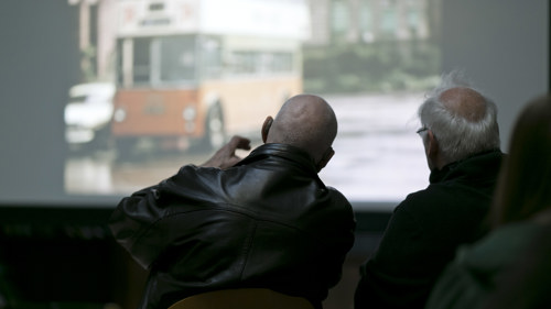 Two community member sit facing a slide show of historic images. 