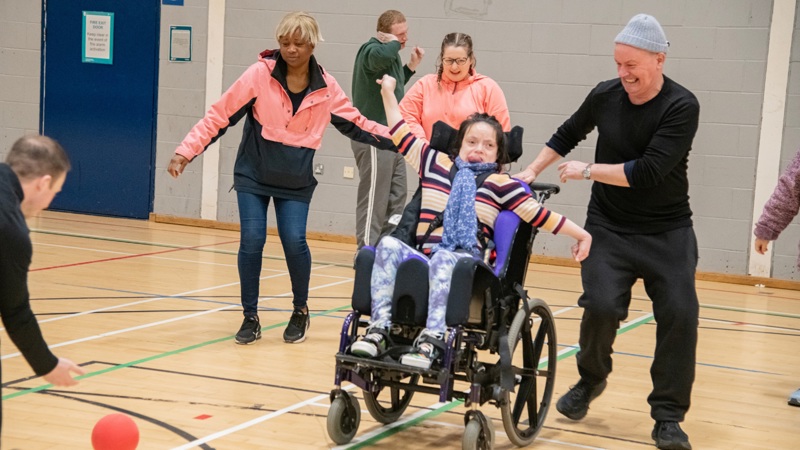 A person in a wheelchair is on a sports court with others surrounding them. They are engaged in a sport together.