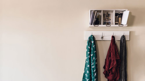 A set of coat hooks on a wall with scarves and jackets hanging off them