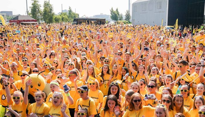 a crowd of people dressed in yellow looking happy and cheering as they set off on a charity walk together