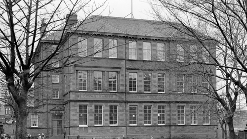 Black and white photo of Govan Parish Church Street Public School with bare tree branches coming in from the sides and children playing in the playground.