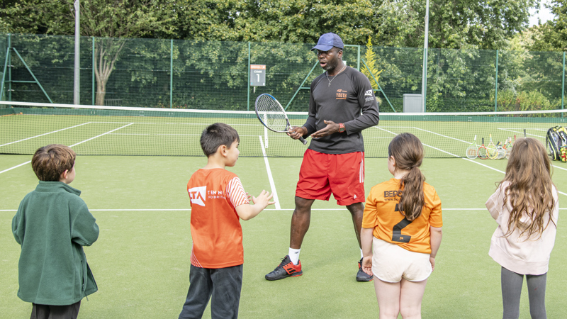 A group of children receiving tennis coaching from coach at Kelvingrove tennis courts.