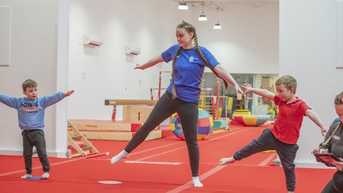 A gymnastics instructor showing two children how to do a balance during a session