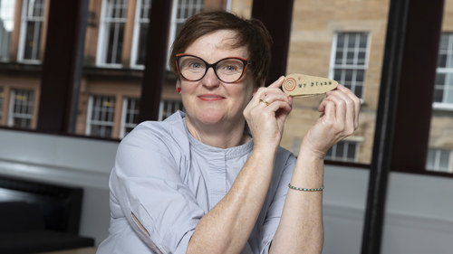 A smiling woman displays a small wooden artwork