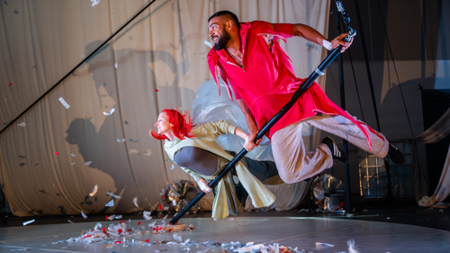 Two performers on a stage performing a flying scene using wires and large poles