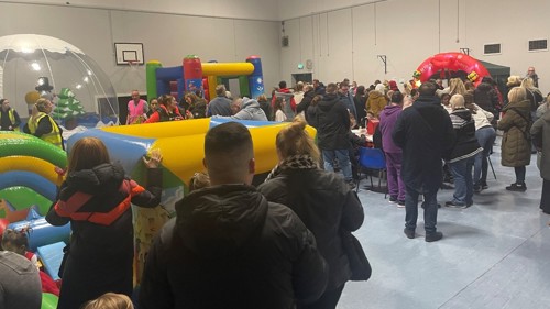 Families enjoying a Christmas fair in a community centre hall with bouncy castle and large inflatable snow globe