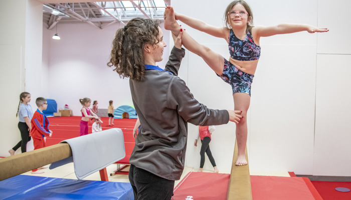 girl balancing on beam with coach assistance