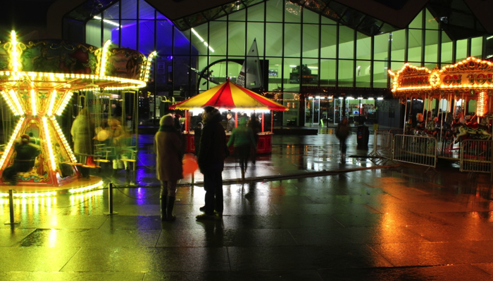 christmas outdoor fair with rides set up outside a museum. the ride are lit up colourfully