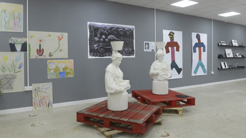 Two statues of "mother Glasgows" are displayed on red pallets. In the background there are painting and prints. 