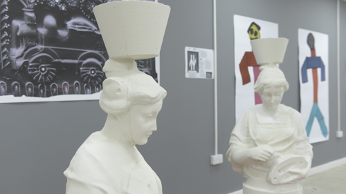 Two statues of "mother Glasgows" are displayed on red pallets. In the background there are painting and prints. 