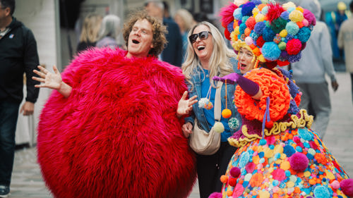 Costumed characters laugh alongside a person with blonde hair and blue jacket