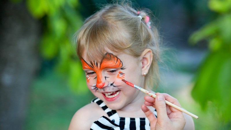 A child smiles widely as they have an orange butterfly painted onto their face.