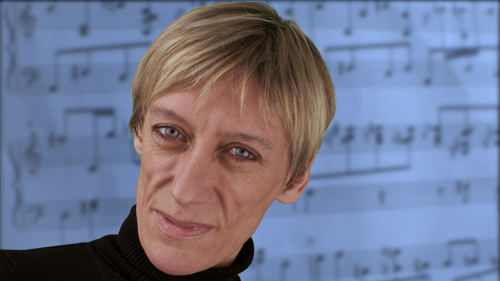 A close up of an Karen McIver's face, they are smiling at the camera and have a blonde pixie cut.