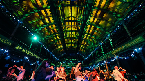 People are dancing during a ceilidh in a warmly lit live music venue 