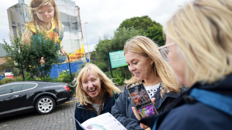 Three people stand in front of a mural using an app and map.