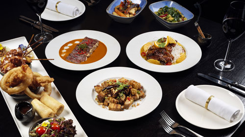 Black table with white crockery and silverware showcasing meals from the menu.