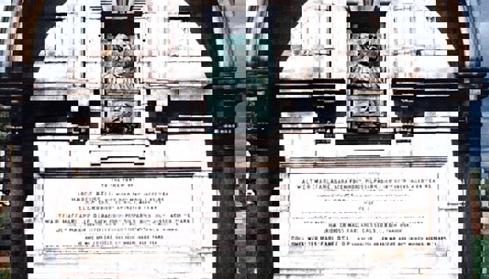 A photograph of a large memorial for Walter MacFarlane which has pillars holding an arch up over a face that has oxidised and turned turquoise.